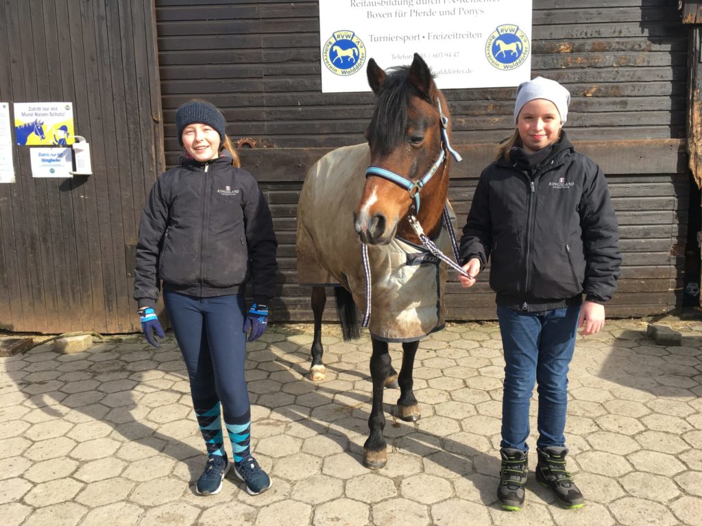 Zwei Mädchen stehen neben einem Pony