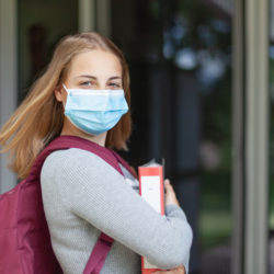 Mädchen mit Maske und Ordner vor Schule