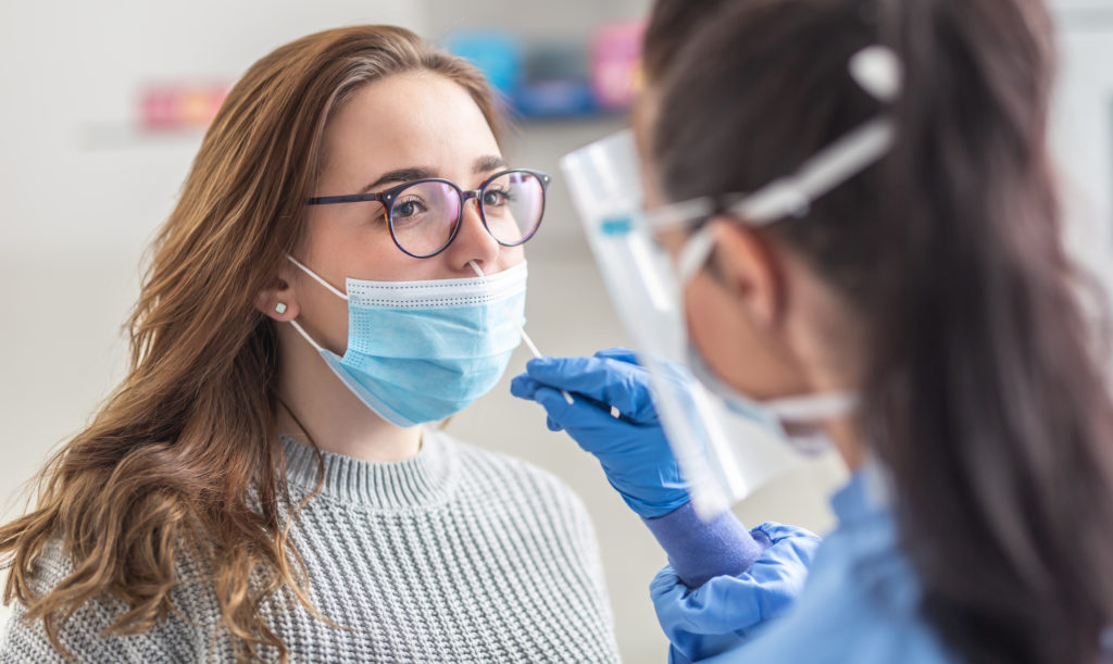 Female patient wearing mask over mouth is having sample taken from nose for a pcr test for Covid 19.