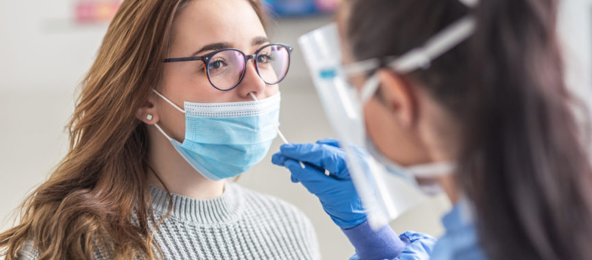 Female patient wearing mask over mouth is having sample taken from nose for a pcr test for Covid 19.