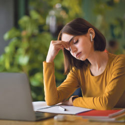 Exhausted young woman using earpods and laptop at cafe