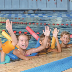 Little kids with swimming noodles in indoor pool